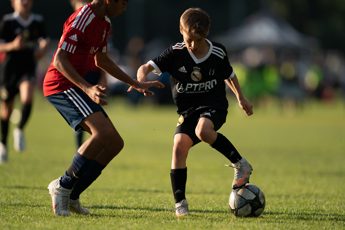 Male LWPFC player, wearing the club's all-black uniform, running with the ball at a summer tournament